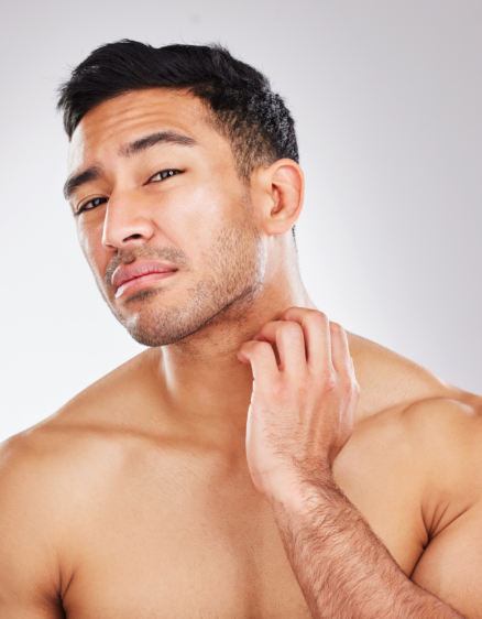 Portrait of a young man checking his skin and looking unhappy during his skincare routine against a grey background