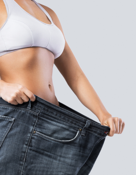 Woman showing result after weight loss wearing on old jeans on gray background